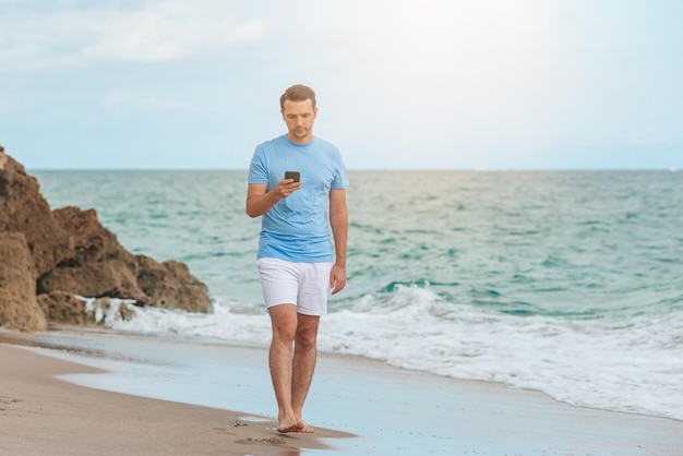 Giovane che tiene il telefono cellulare in mano mentre si cammina sulla spiaggia