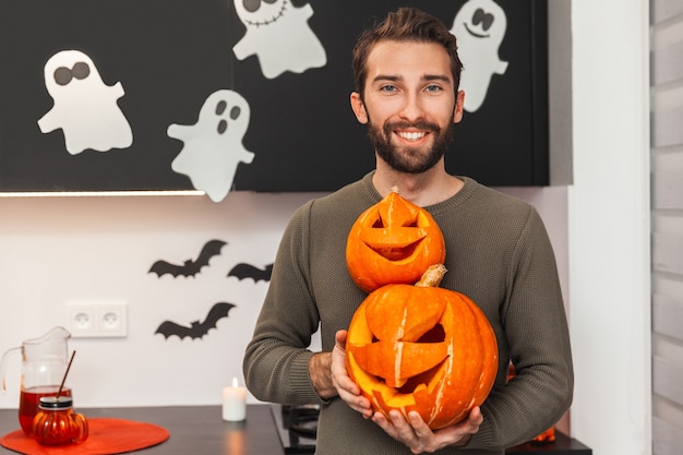 Giovane che tiene le zucche per halloween e guarda la telecamera