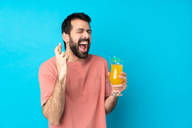 Giovane che tiene un cocktail sopra la parete blu isolata con l'incrocio delle dita