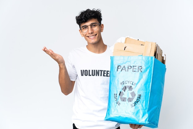 Giovane che tiene un sacchetto di riciclaggio pieno di carta che estende le mani a lato per invitare a venire