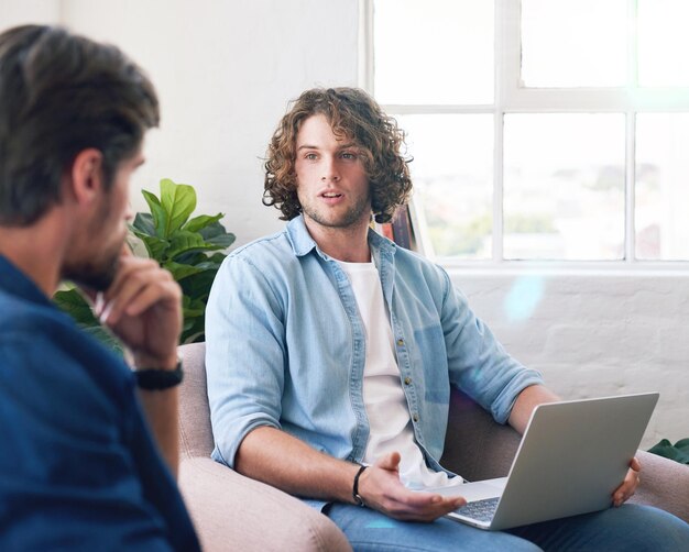 Giovane che usa il laptop in chat con un amico che fa brainstorming su idee per il progetto seduto sul divano di casa