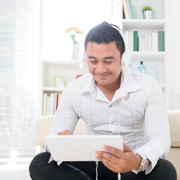 Giovane che usa un tablet digitale mentre ascolta musica con le cuffie a casa