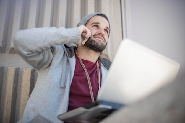 Giovane che utilizza il telefono cellulare e il computer portatile all'aperto