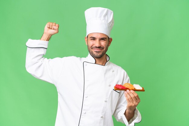 Giovane chef caucasico tenendo un sushi su sfondo isolato facendo un gesto forte