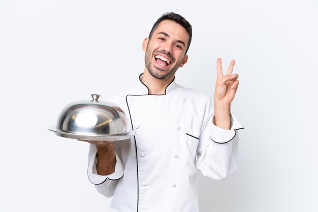 Giovane chef con vassoio isolato su sfondo bianco sorridente e mostrando il segno della vittoria