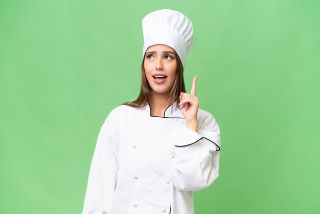Giovane chef donna caucasica su sfondo isolato pensando un'idea puntando il dito verso l'alto