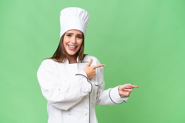 Giovane chef donna caucasica su sfondo isolato sorpreso e indicando il lato