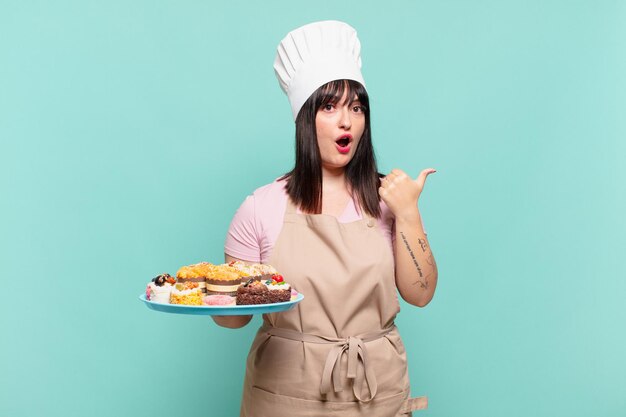 Giovane chef donna che sembra stupita per l'incredulità, indicando un oggetto sul lato e dicendo wow, incredibile