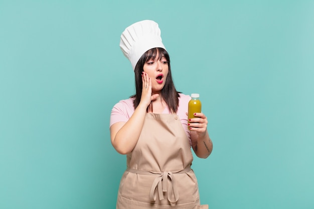 Giovane chef donna che si sente felice, eccitata e sorpresa, guardando di lato con entrambe le mani sul viso