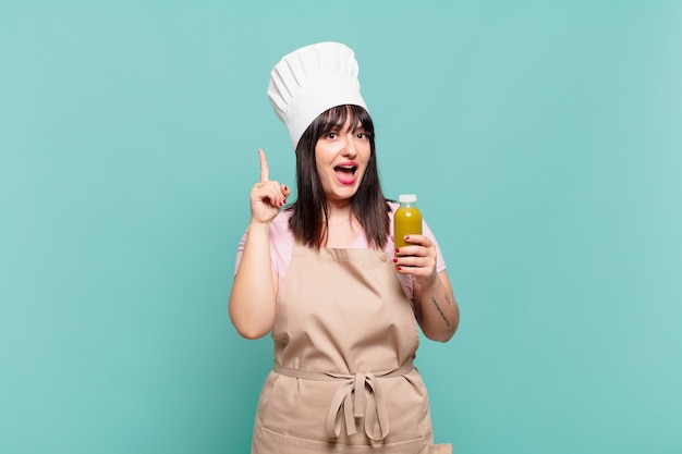Giovane chef donna che si sente un genio felice ed eccitato dopo aver realizzato un'idea, alzando allegramente il dito, eureka!