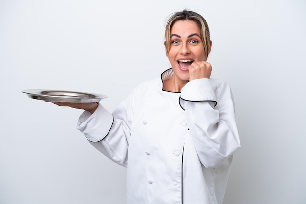 Giovane chef donna con vassoio isolato su sfondo bianco che celebra una vittoria in posizione di vincitore