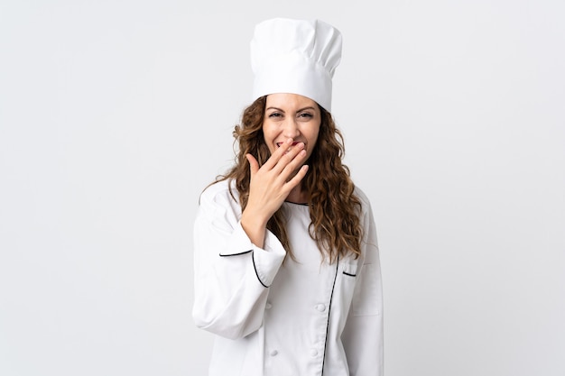 Giovane chef donna isolata sulla parete bianca felice e sorridente che copre la bocca con la mano