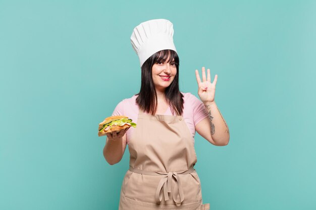 Giovane chef donna sorridente e dall'aspetto amichevole, mostrando il numero quattro o il quarto con la mano in avanti, conto alla rovescia