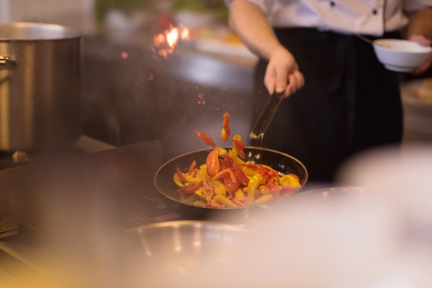 Giovane chef maschio che lancia le verdure nel wok in una cucina commerciale