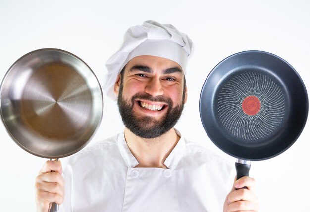 Giovane chef maschio che mostra una padella inossidabile e una padella antiaderente mentre sorride e guarda la fotocamera