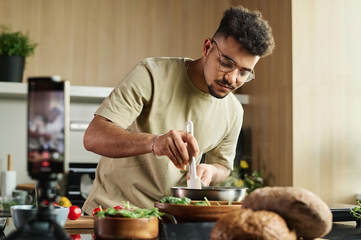 Foto giovane chef mediorientale che mescola il cibo in padella con una spatola mentre fa un video sullo smartphone