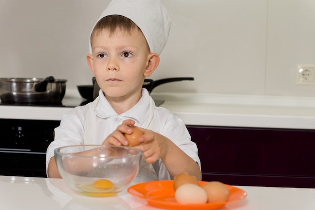 Giovane chef rompe le uova in una ciotola in cucina