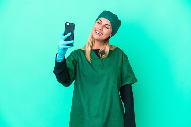 Giovane chirurgo donna uruguaiana in uniforme verde isolata su sfondo blu che fa un selfie