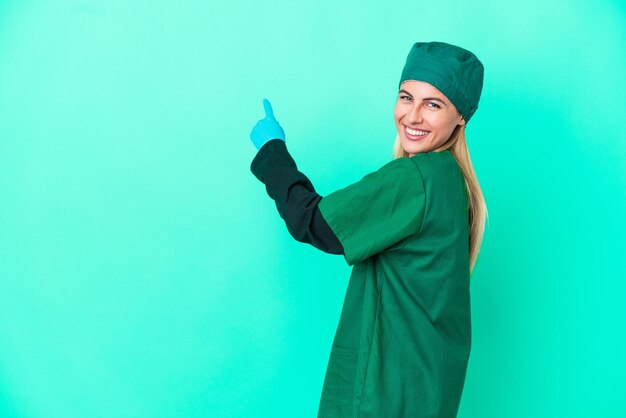 Giovane chirurgo Donna uruguaiana in uniforme verde isolata su sfondo blu che punta indietro