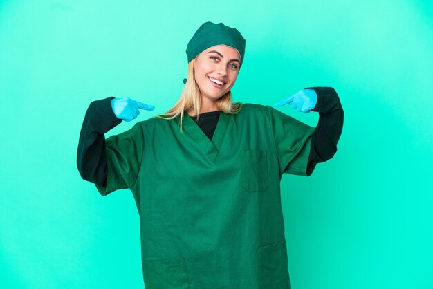 Giovane chirurgo donna uruguaiana in uniforme verde isolata su sfondo blu orgogliosa e soddisfatta