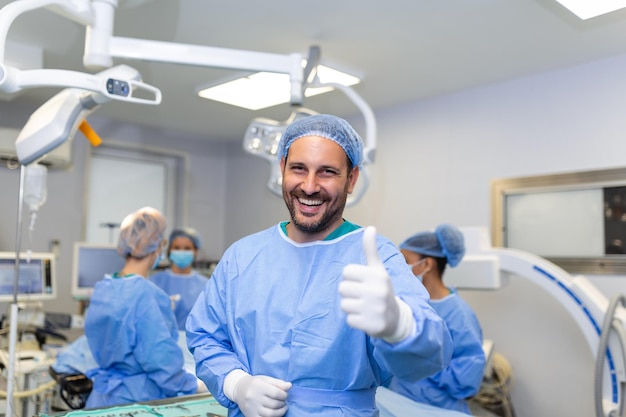 Giovane chirurgo maschio in piedi in sala operatoria che mostra i pollici in su pronto a lavorare su un paziente Uniforme chirurgica per operatori sanitari maschi in sala operatoria