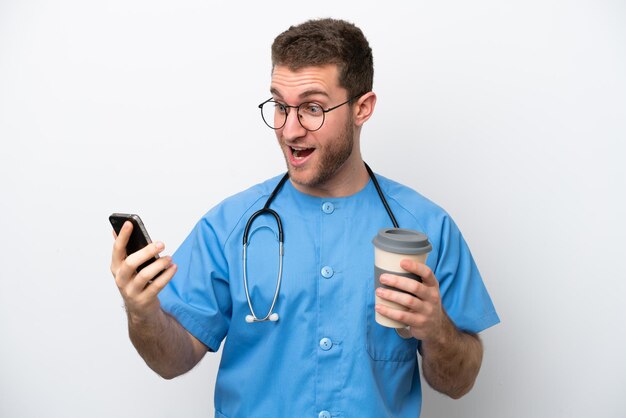 Giovane chirurgo medico uomo caucasico isolato su sfondo bianco tenendo il caffè da portare via e un cellulare