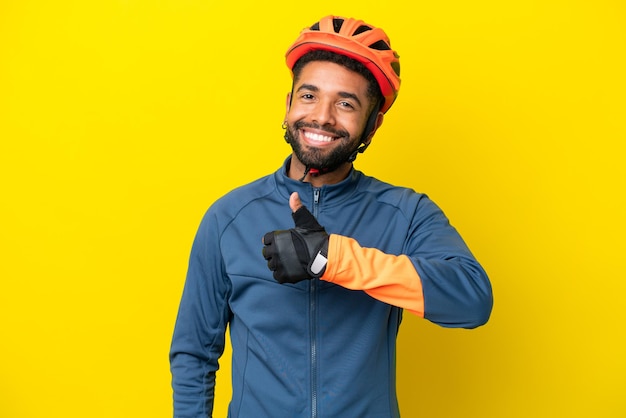 Giovane ciclista brasiliano uomo isolato su sfondo giallo dando un pollice in alto gesto