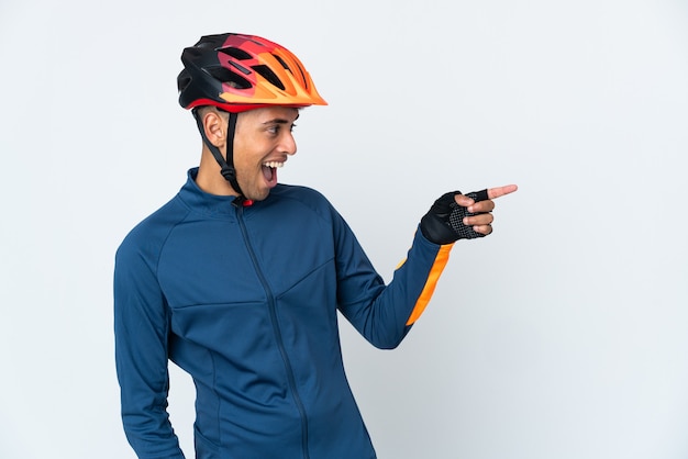 Giovane ciclista brasiliano uomo isolato sul muro bianco che punta il dito di lato e presenta un prodotto