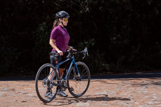 Giovane ciclista che riposa con la sua bicicletta sul ciglio della strada indossando casco e occhiali da sole