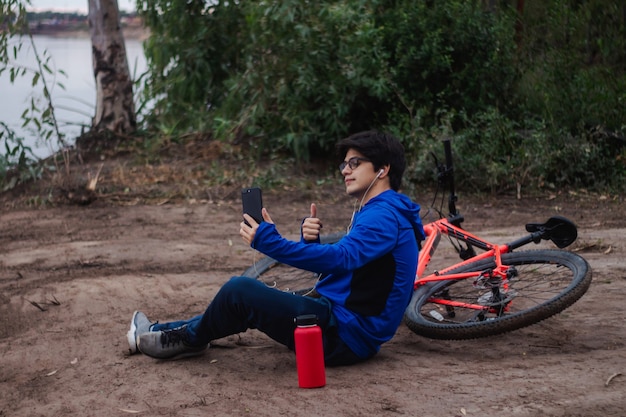 Giovane ciclista che si fa un selfie, appoggiato a terra accanto alla sua bici