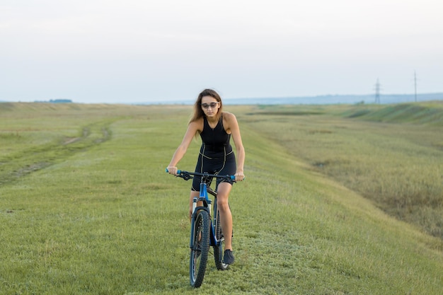 Giovane ciclista femminile in bicicletta sulla strada rurale vista laterale