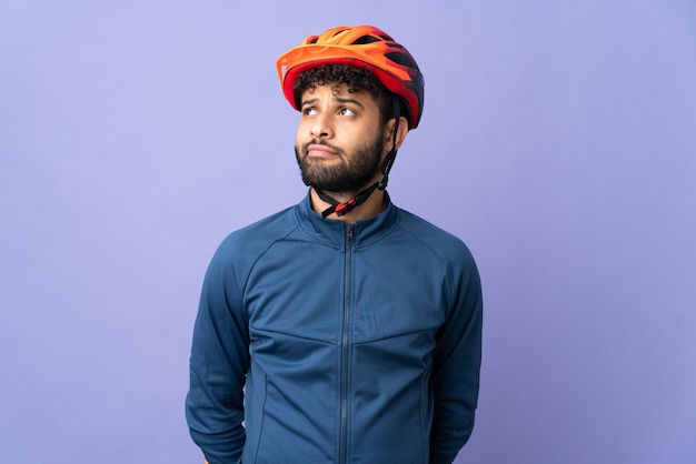 Giovane ciclista marocchino uomo isolato su sfondo viola e alzando lo sguardo