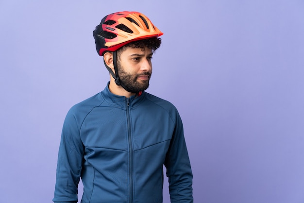 Giovane ciclista marocchino uomo isolato su viola guardando al lato