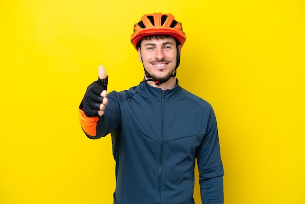 Giovane ciclista uomo caucasico isolato su sfondo giallo con i pollici in su perché è successo qualcosa di buono