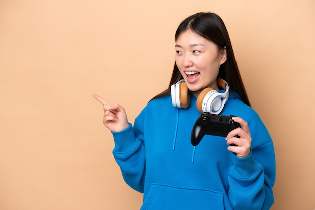 Giovane cinese che gioca con un controller per videogiochi isolato su sfondo beige che punta il dito di lato e presenta un prodotto