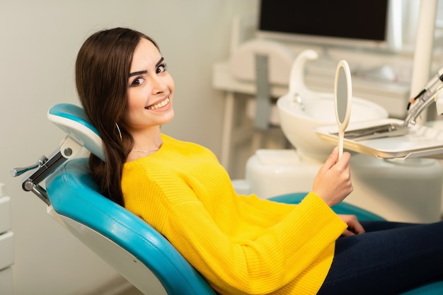 Giovane cliente felice della donna che esamina lo specchio con il sorriso a trentadue denti all'ufficio dentale