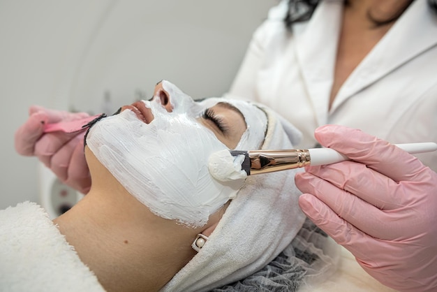 Giovane cliente femminile che riceve un trattamento viso dalla maschera bianca nel salone di bellezza termale Concetto di cura della pelle