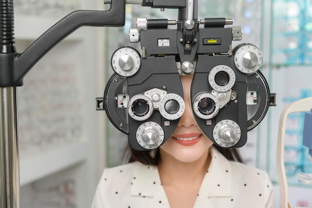 Giovane cliente femminile che viene esaminata test visivo utilizzando il dispositivo di misurazione della vista optometria bifocale da parte di un oftalmologo nel concetto di cura degli occhi del centro ottico