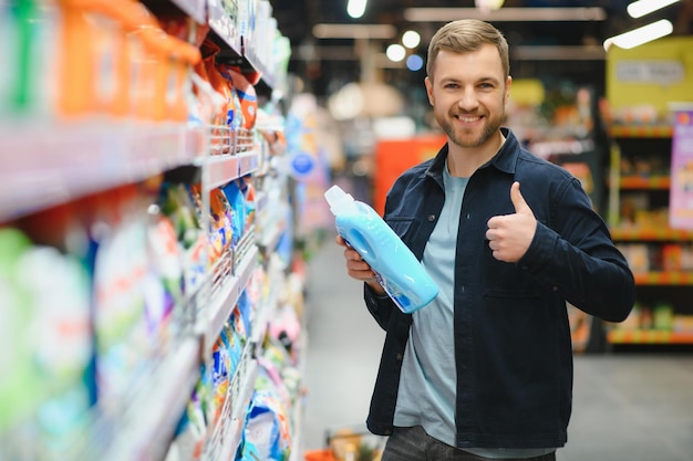 Giovane cliente maschio positivo allegro che fa acquisti nel supermercato che compra prodotti chimici per la casa