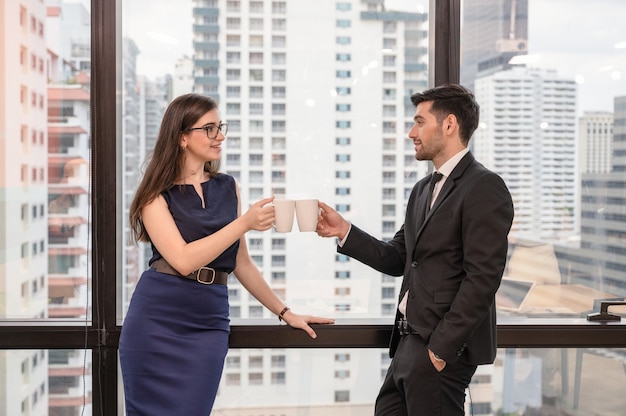 Giovane collega caucasico di affari che tiene e applaude la tazza di caffè in ufficio