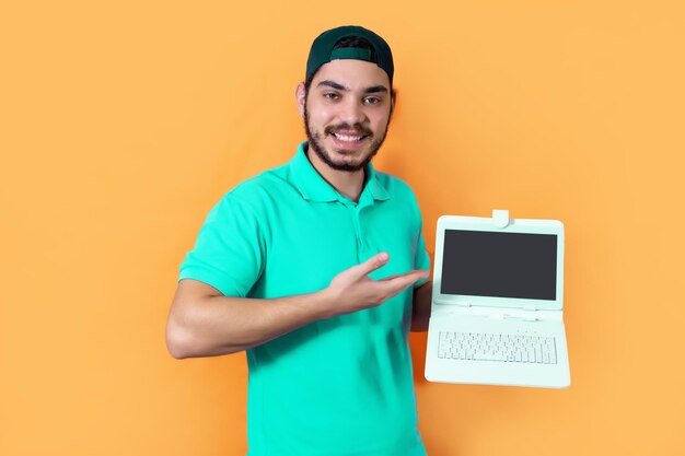 Giovane con barba Tshirt e cappuccio verde che mostra alla fotocamera un tablet con tastiera su sfondo giallo
