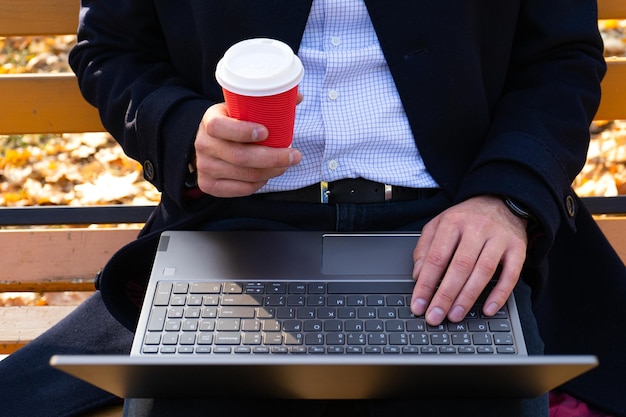 Giovane con caffè e utilizzando il laptop nella vista dall'alto del parco autunnale