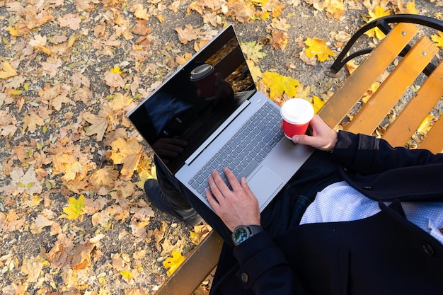 Giovane con caffè e utilizzando il laptop nella vista dall'alto del parco autunnale