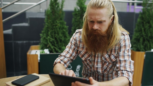 Giovane con computer tablet seduto nella caffetteria all'aperto avendo relax e riposo di lavoro