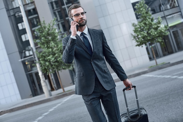 Giovane con gli occhiali che parla al telefono mentre si cammina all'aperto