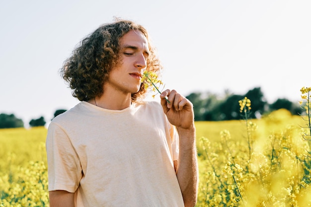 giovane con i capelli ricci con un fiore nel naso in un campo di colza in una giornata di sole primaverile