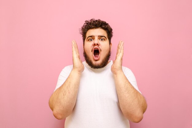 giovane con i capelli ricci e la barba con la faccia scioccata che esamina la macchina fotografica