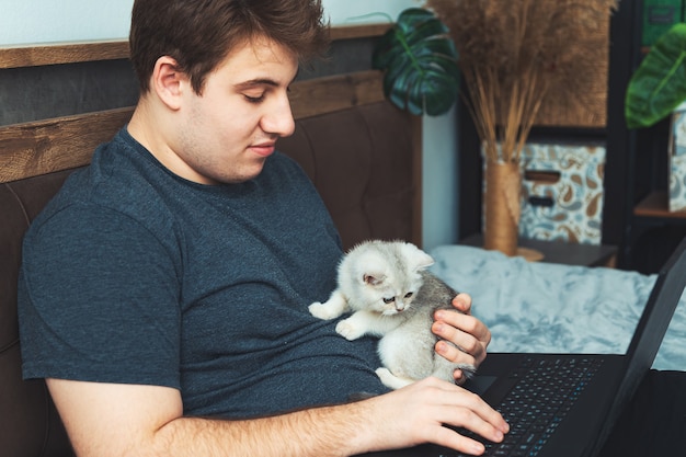 Giovane con il gattino che lavora al suo computer portatile. Il concetto di apprendimento e lavoro online.