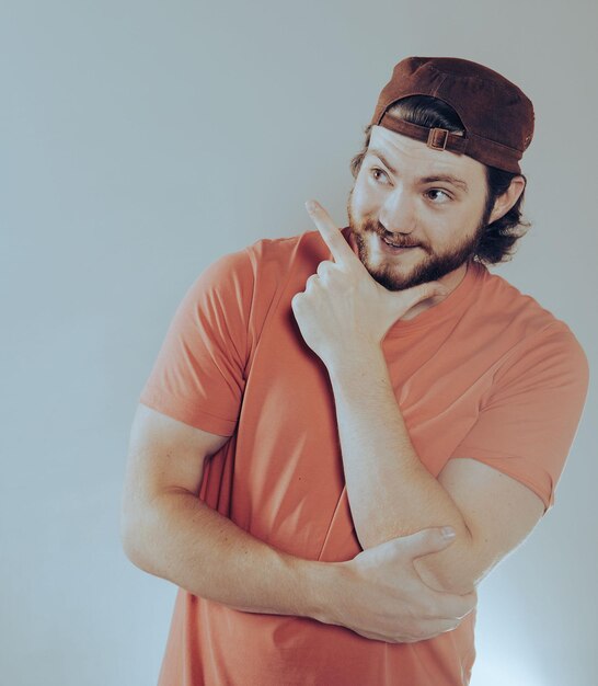 Giovane con la barba che indossa un cappello allegro che indica con la mano e il dito verso il lato