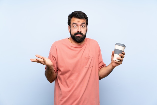 Giovane con la barba che tiene un caffè da asporto sopra la parete blu isolata che fa gesto di dubbi